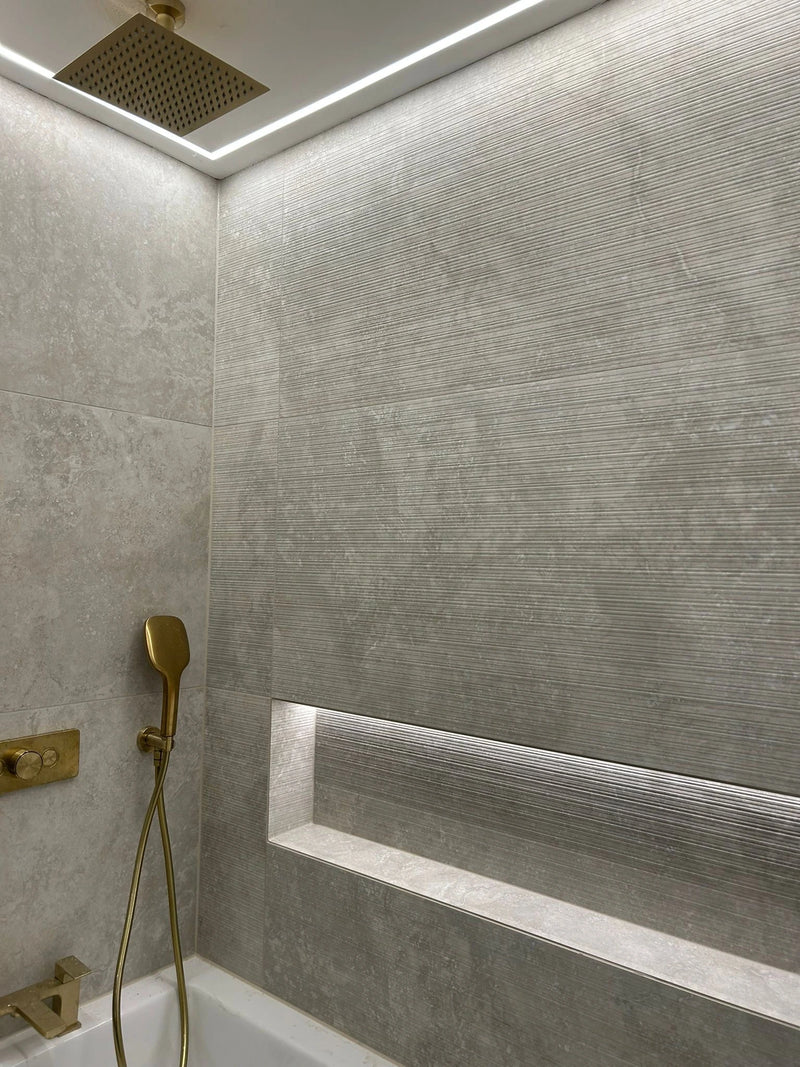 Modern bathroom shower with gray tiles, gold fixtures, and a built-in shelf.