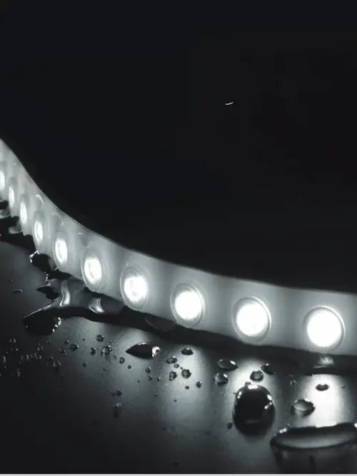LED light strip on a reflective black surface with water droplets.