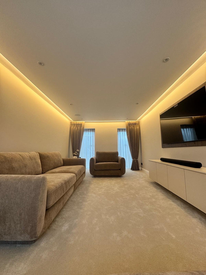 Modern living room with beige sofa, armchair, and TV setup. LED Lighting in the coving giving the room a soft elegant glow.
