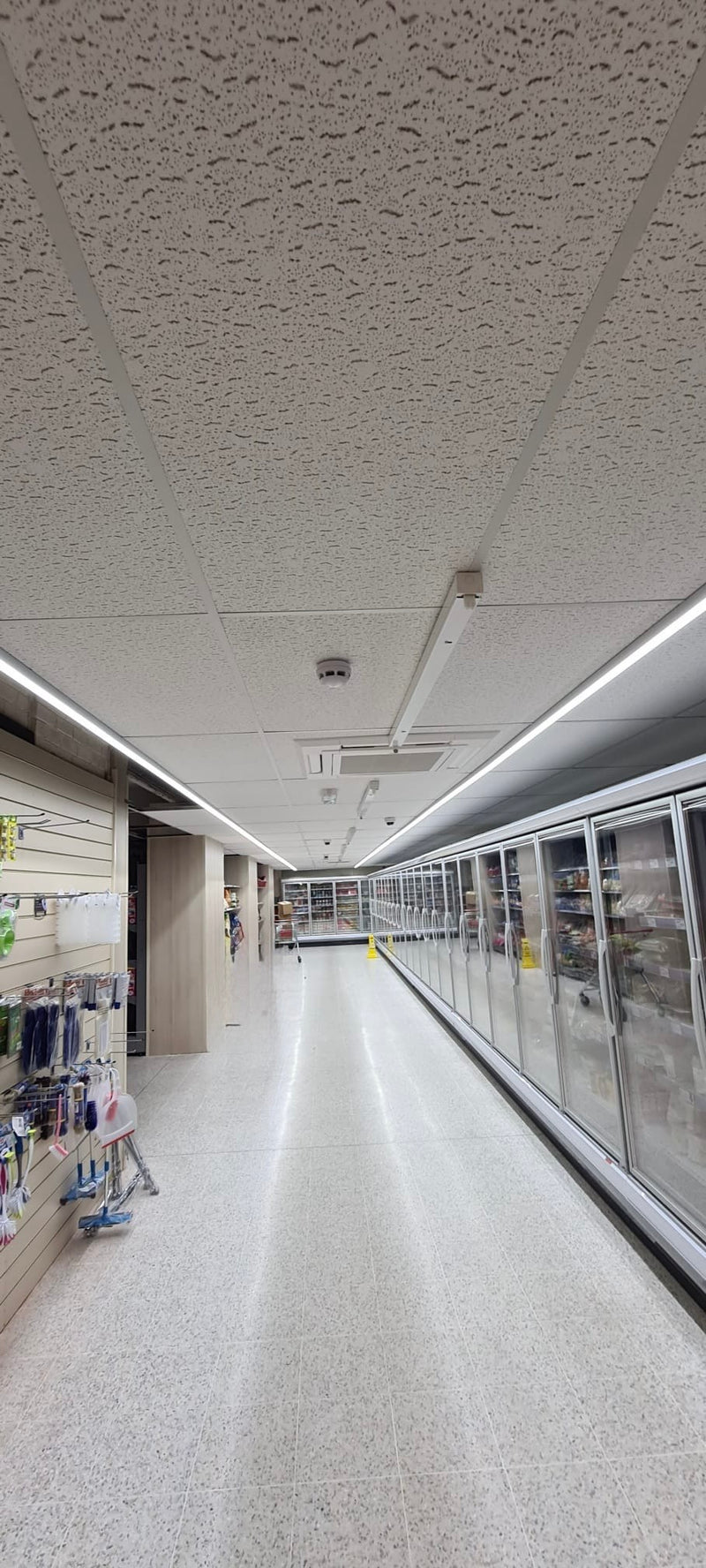 Supermarket aisle with refrigerated shelves and ceiling lights.
