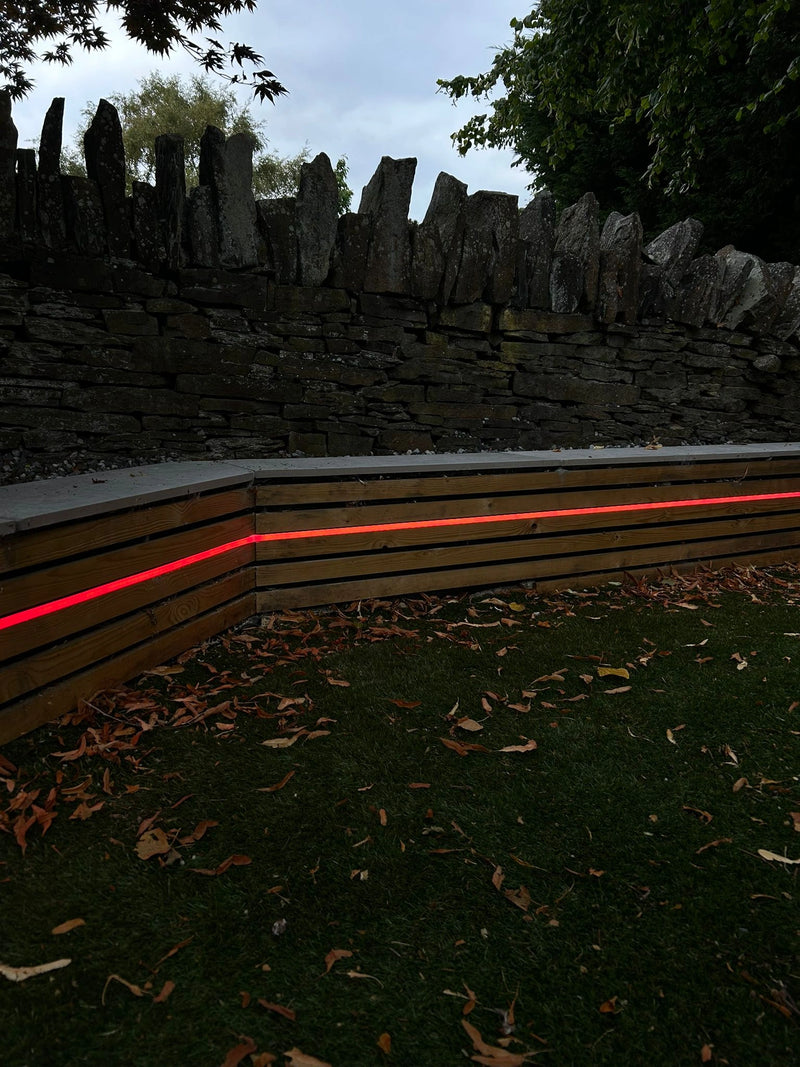 Red laser light on a wooden bench against a stone wall and trees