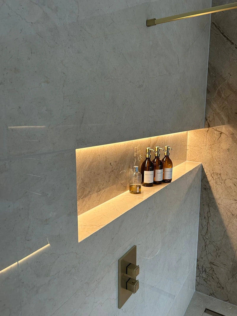 Bottles on a ledge in a modern bathroom with marble walls and lighting.