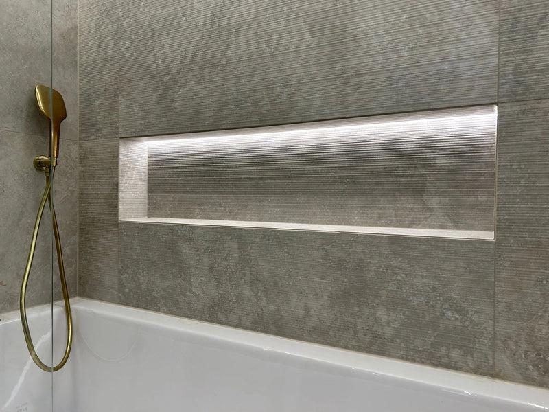 Modern bathroom with a bathtub, gold shower head, and gray tiled wall.